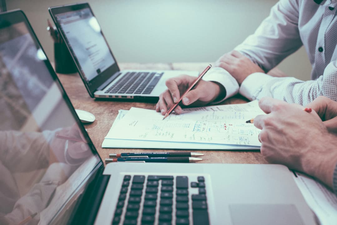 Two professionals reviewing documents with laptops on a desk, highlighting detailed financial planning and analysis.