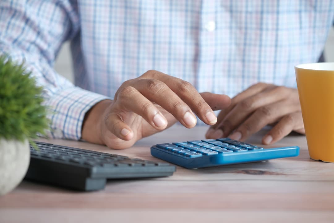 A professional using a calculator on a wooden desk, showcasing hands-on financial calculations and planning.