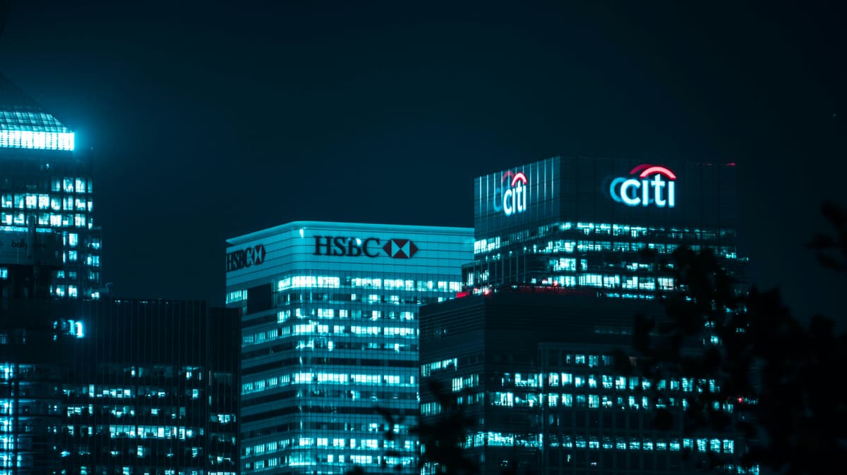 Illuminated corporate buildings at night showcasing the logos of major financial institutions, emphasizing global banking and finance.