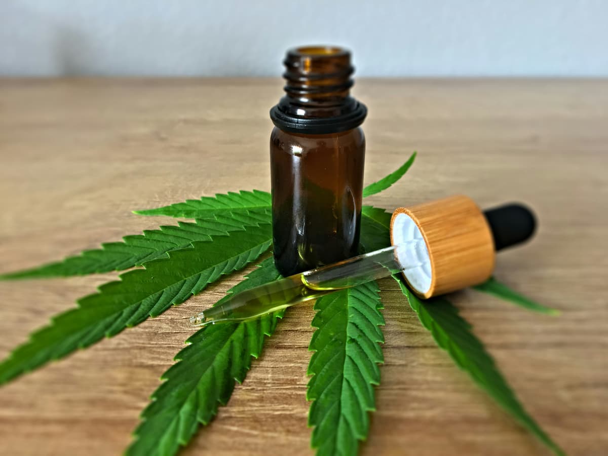 A small amber glass bottle with a dropper placed on top of cannabis leaves, symbolizing natural wellness and CBD oil products.