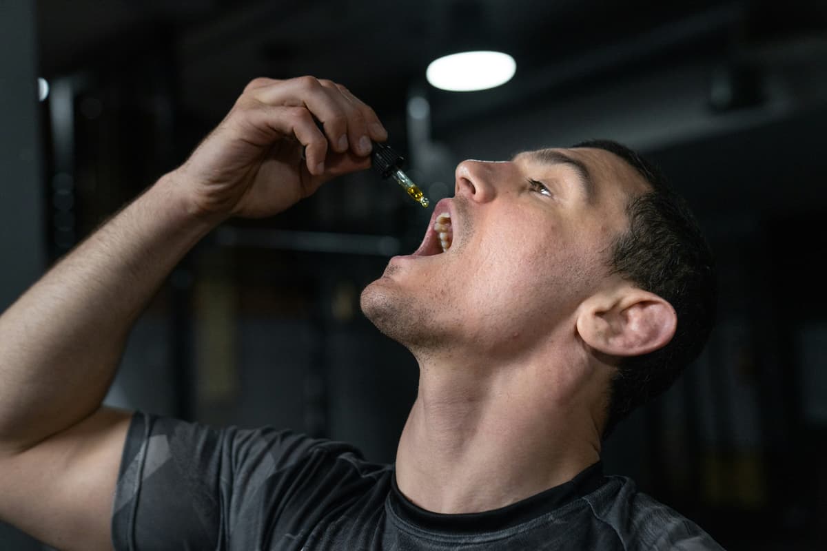 A man taking CBD oil sublingually in a gym setting, representing health, fitness, and recovery through natural supplements.