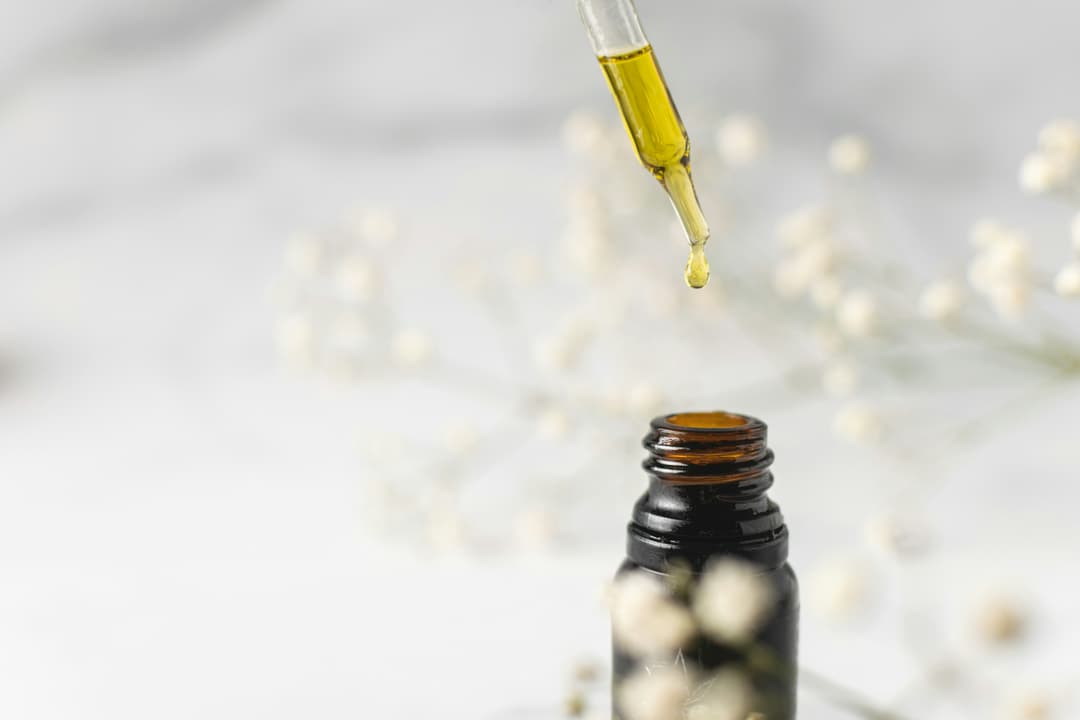 A close-up of a dropper dispensing golden CBD oil into a glass bottle, with soft floral decor in the background, evoking purity and elegance in product presentation.