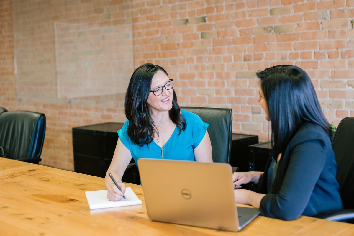 Two women engaging in a professional coaching session with a laptop and notebook in a bright office environment.