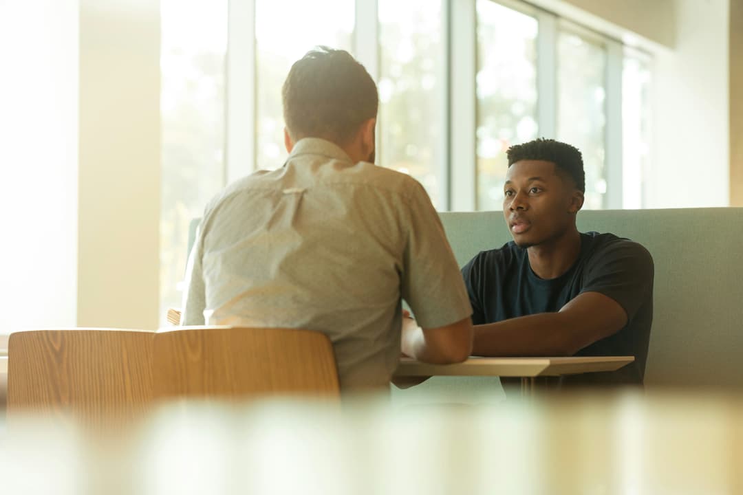 Two individuals having a one-on-one conversation in a modern office setting, symbolizing mentorship and guidance.