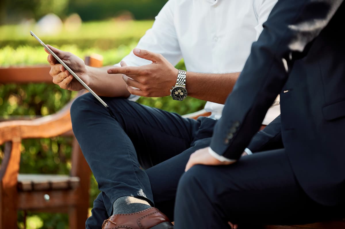 Two professionals in a relaxed outdoor environment discussing ideas on a tablet, emphasizing innovation and teamwork.