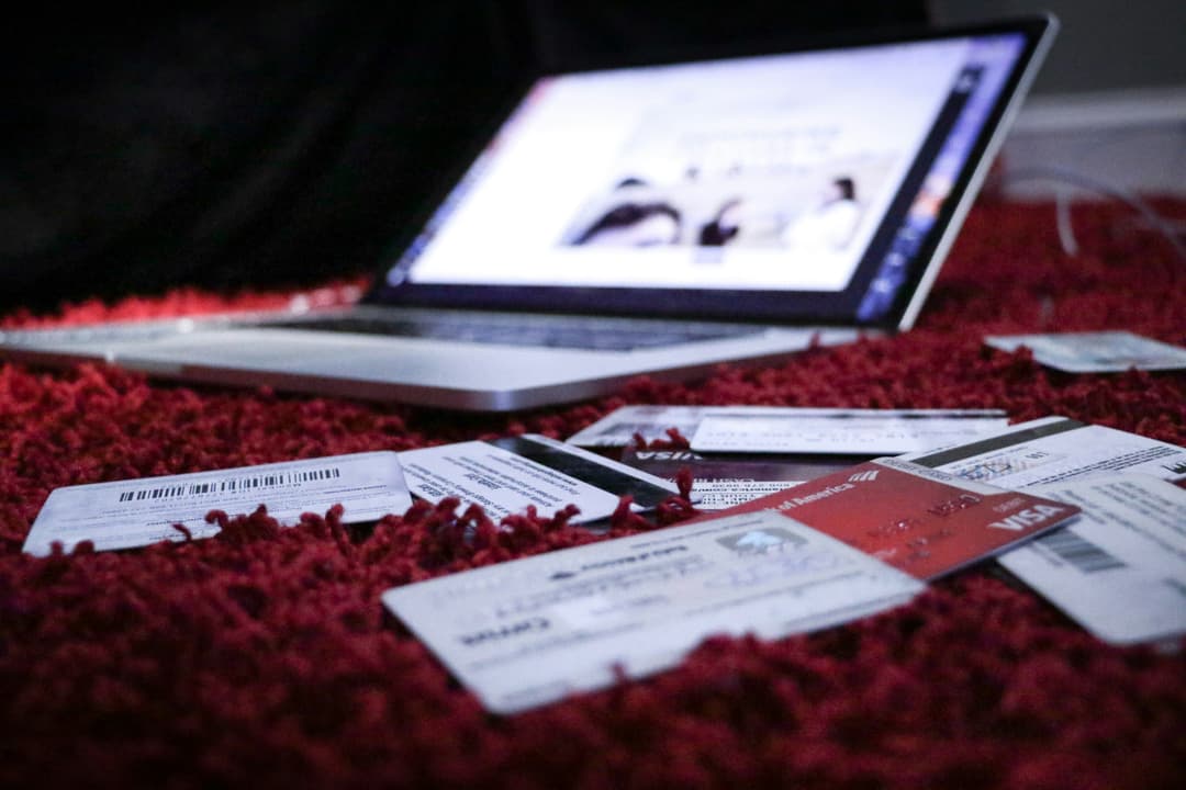 A scattered display of credit cards on a carpet with a laptop in the background, representing financial clutter or online transactions.