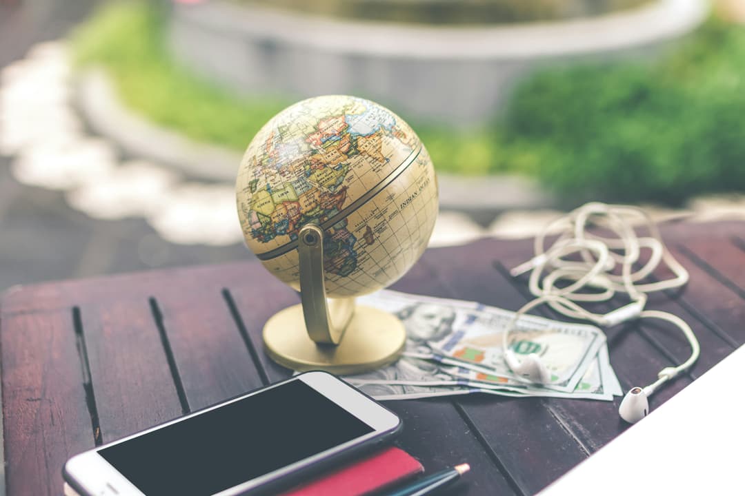 A table setup with a miniature globe, smartphone, cash, and earbuds, representing travel and exploration.