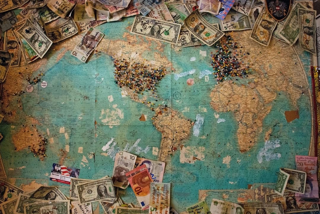 A world map covered with currency notes and colorful pushpins marking various locations, symbolizing global connections.