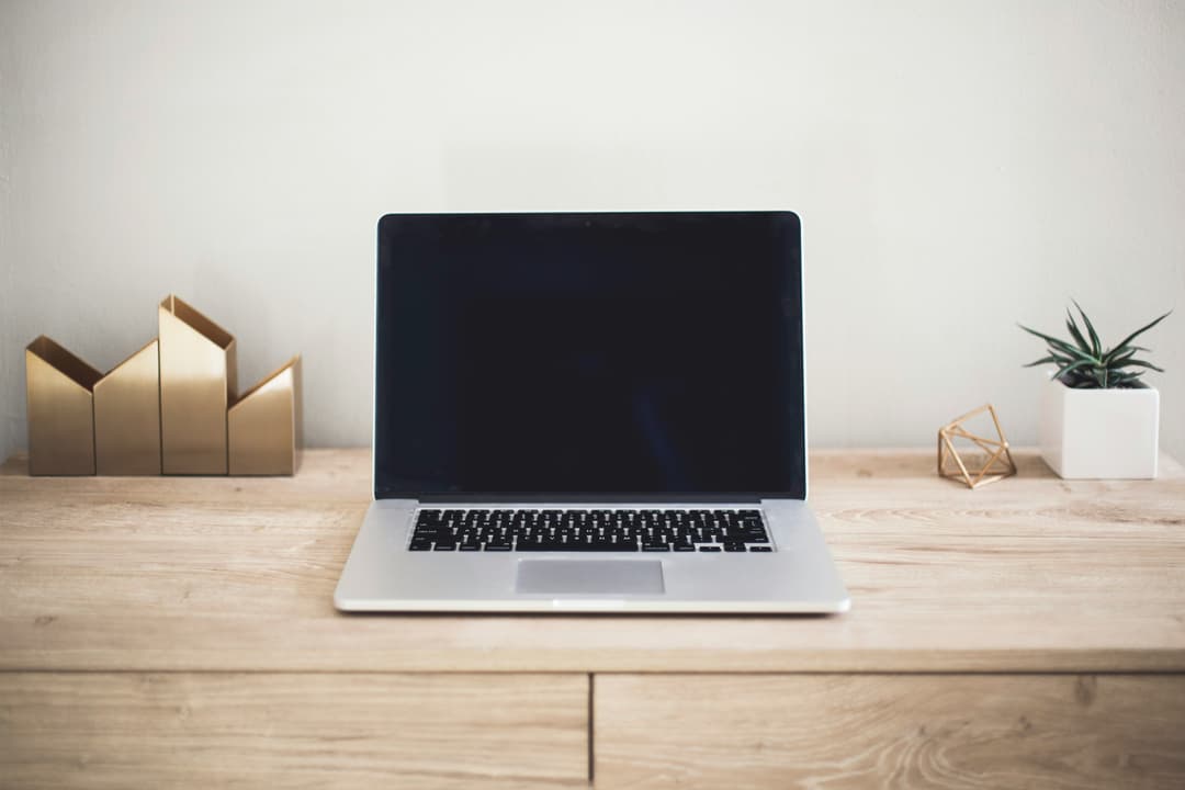 A modern and clean workspace featuring a laptop on a wooden desk with golden decor and a small plant.