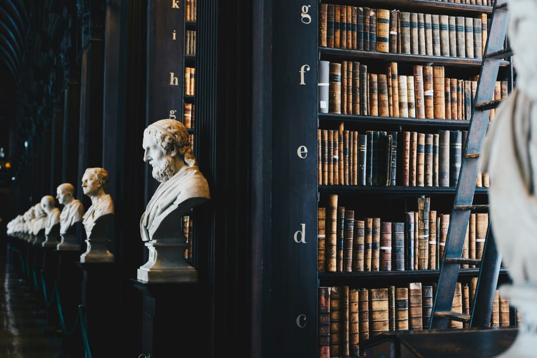 A historic library with rows of marble busts and shelves filled with leather-bound books, exuding a sense of tradition and knowledge.