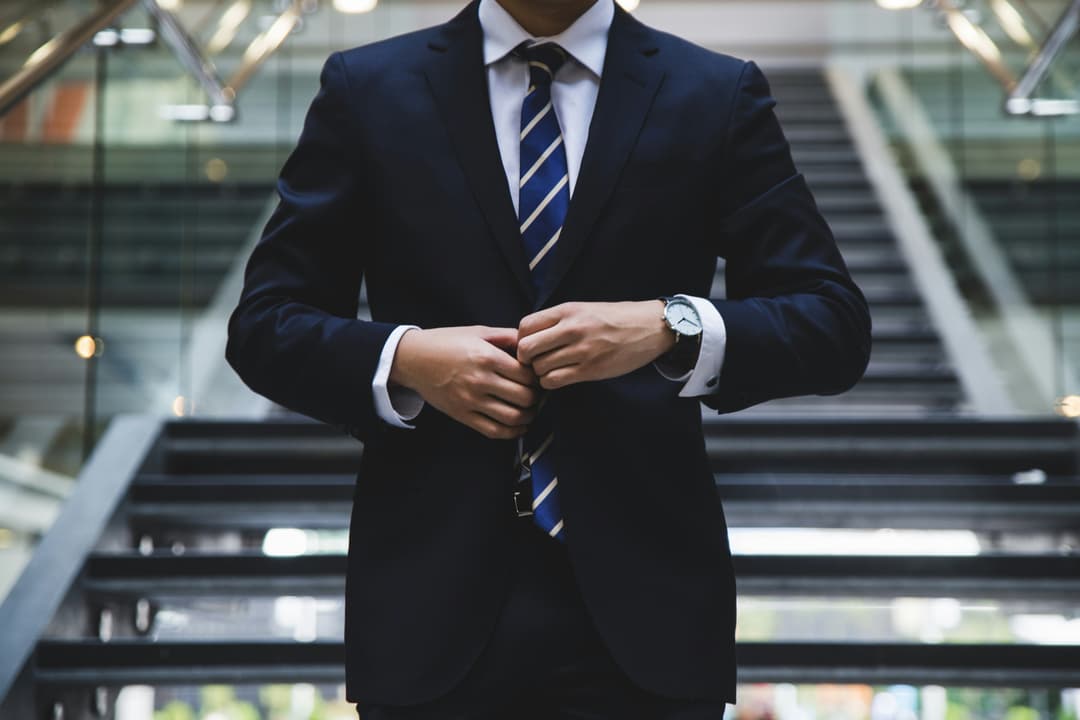 A confident professional in a sharp suit adjusting his jacket, standing on modern office stairs, ready to take on the day.