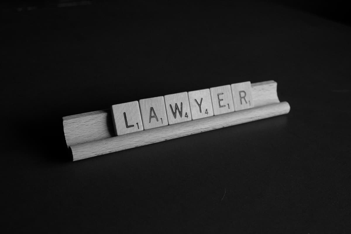 The word 'LAWYER' spelled out using Scrabble tiles against a dark, minimalist background, symbolizing legal expertise.