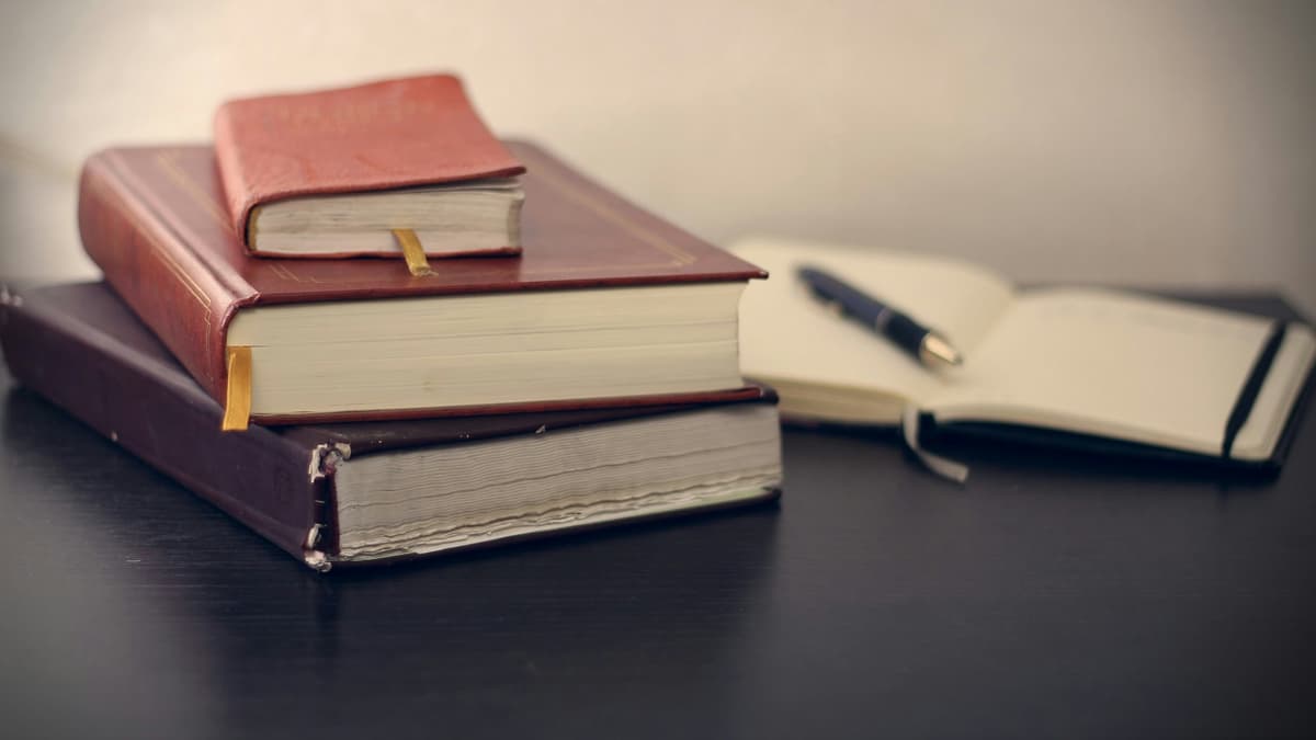 A stack of leather-bound books and an open notebook with a pen, representing research and preparation in the legal field.