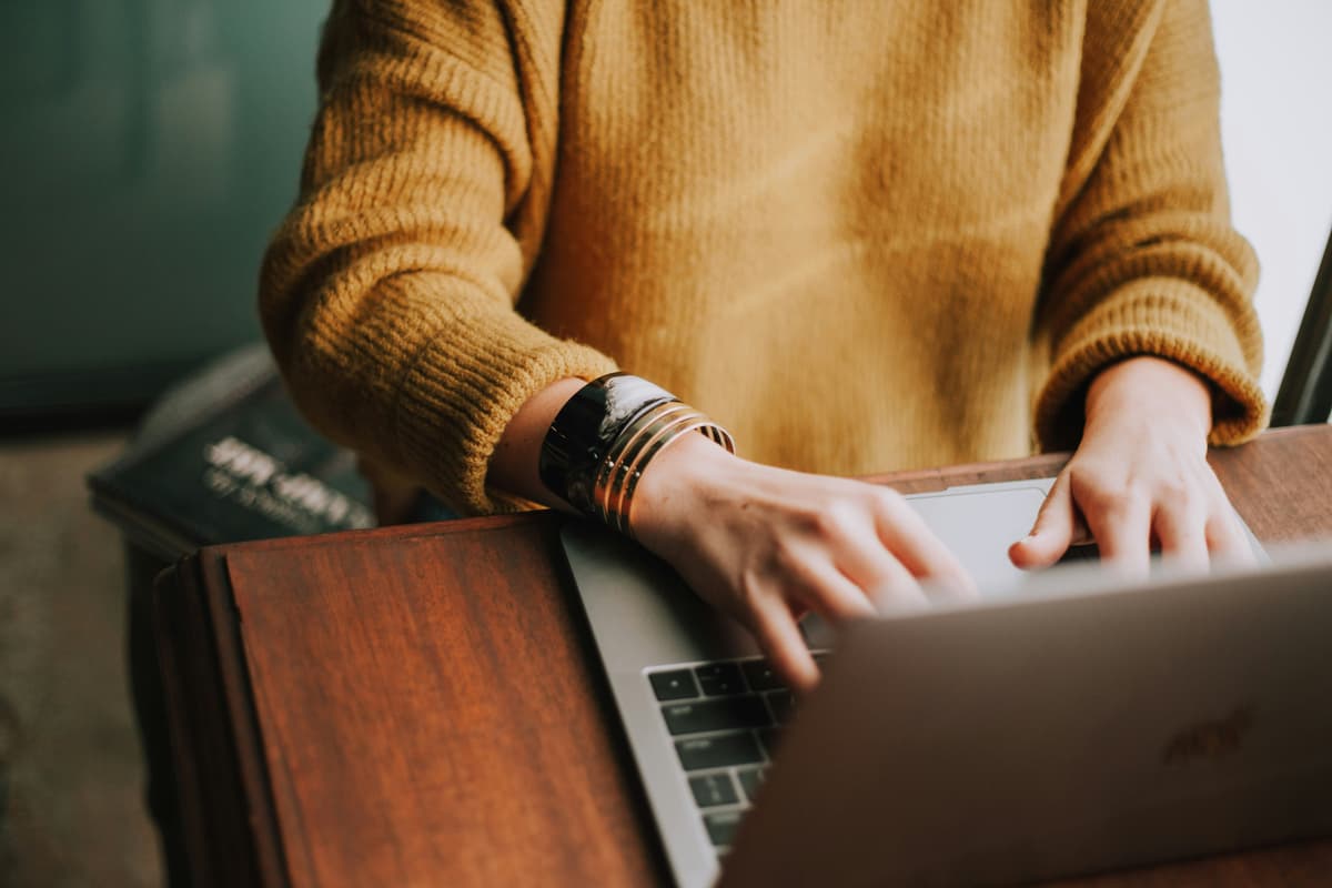 A person typing on a laptop wearing a yellow sweater, representing productivity and online tasks in a cozy environment.