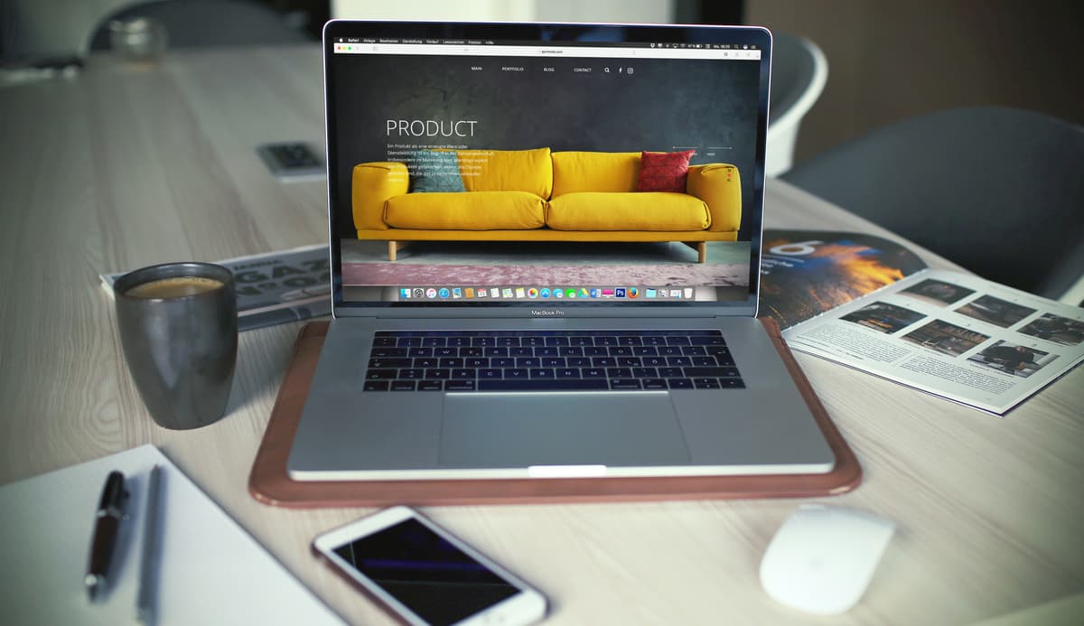 A laptop showcasing a product page with a yellow sofa, accompanied by a coffee cup and smartphone, signifying e-commerce and product marketing.