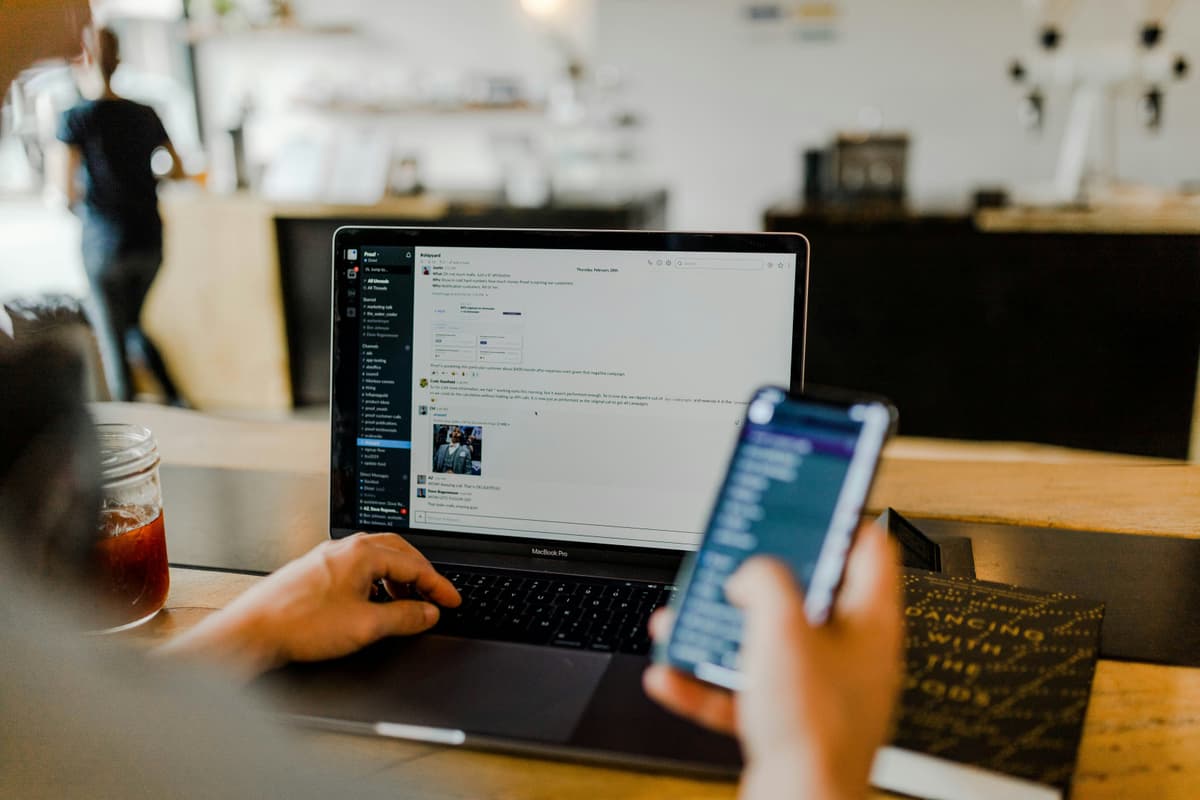 A workspace with a laptop and phone in use, showcasing digital communication and multitasking in a casual environment.