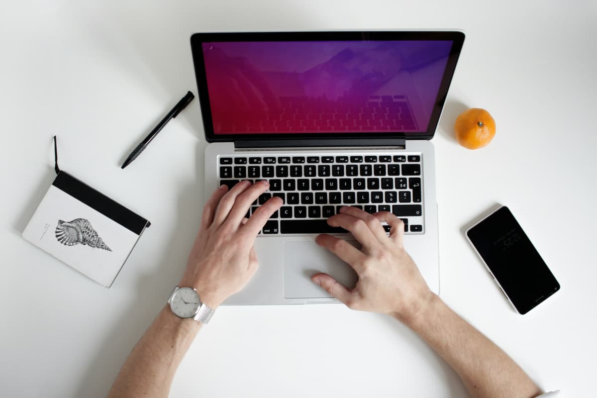 A person typing on a laptop with a clean desk setup, indicating focus and a professional workspace for digital tasks.