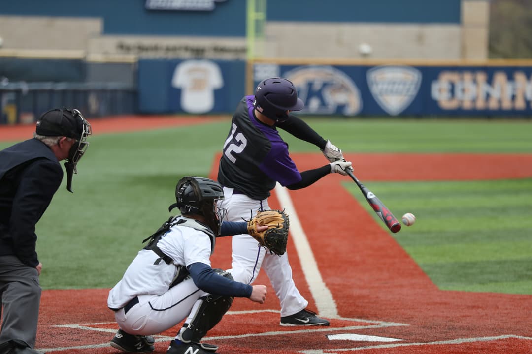 Baseball player mid-swing during a game with a catcher and umpire in action.