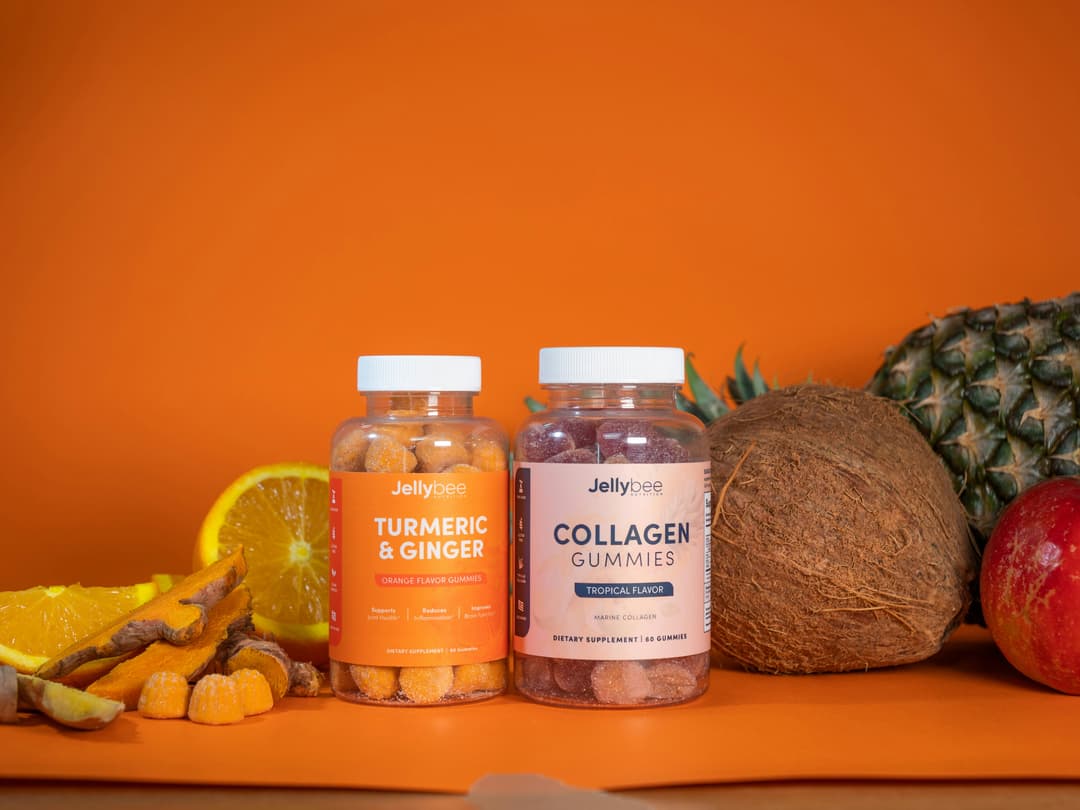 Colorful jars of turmeric and collagen gummies placed amidst tropical fruits, set against a vibrant orange background.