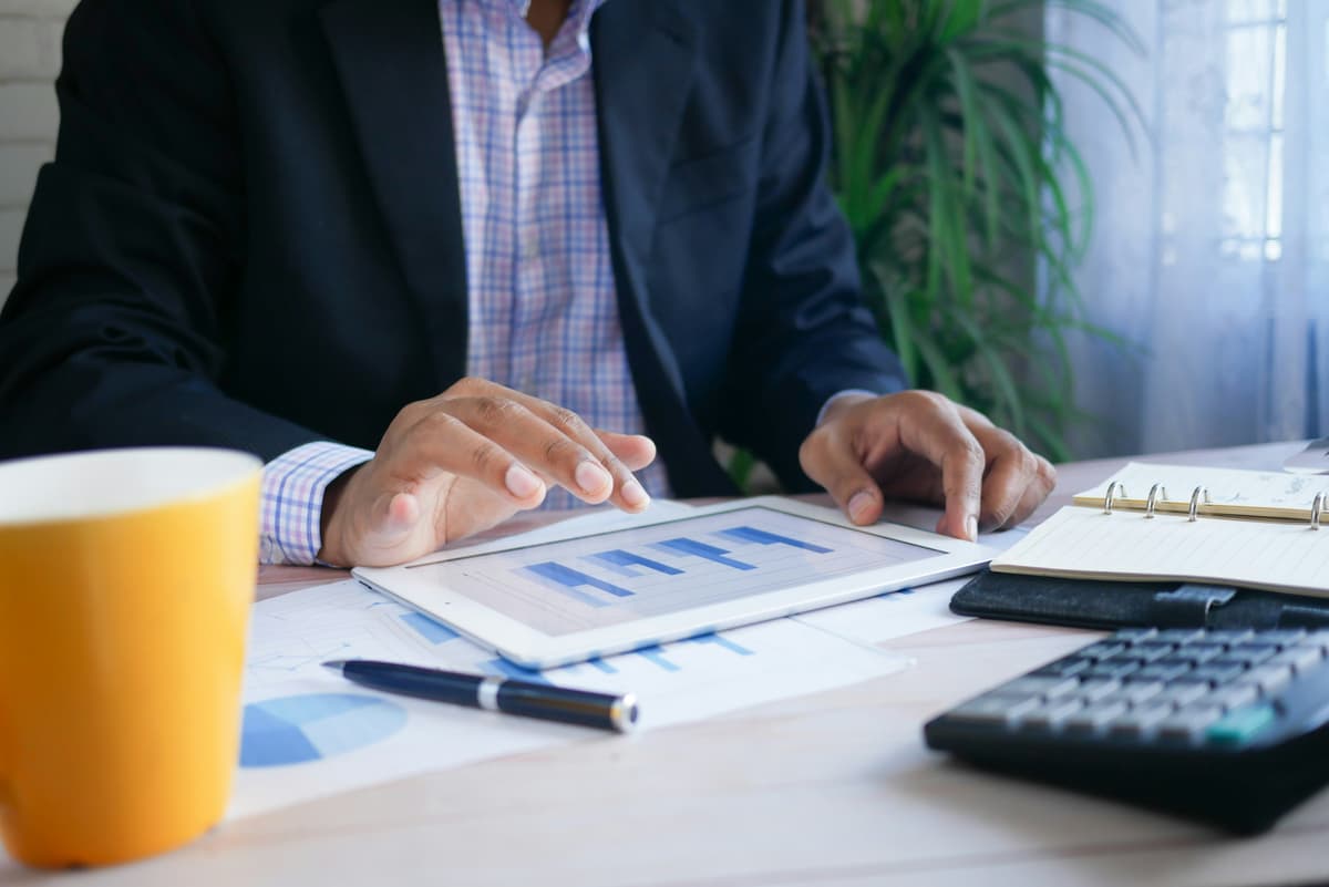 A businessperson analyzing data on a tablet at a desk, indicating strategy and decision-making in a financial or operational context.